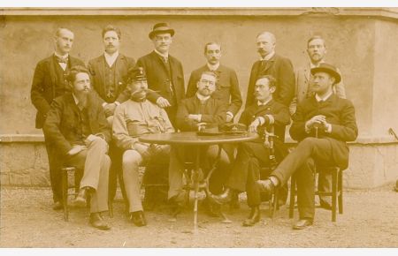 [Gruppenfoto - 11 Männer sitzend u. stehend um runden Tisch].